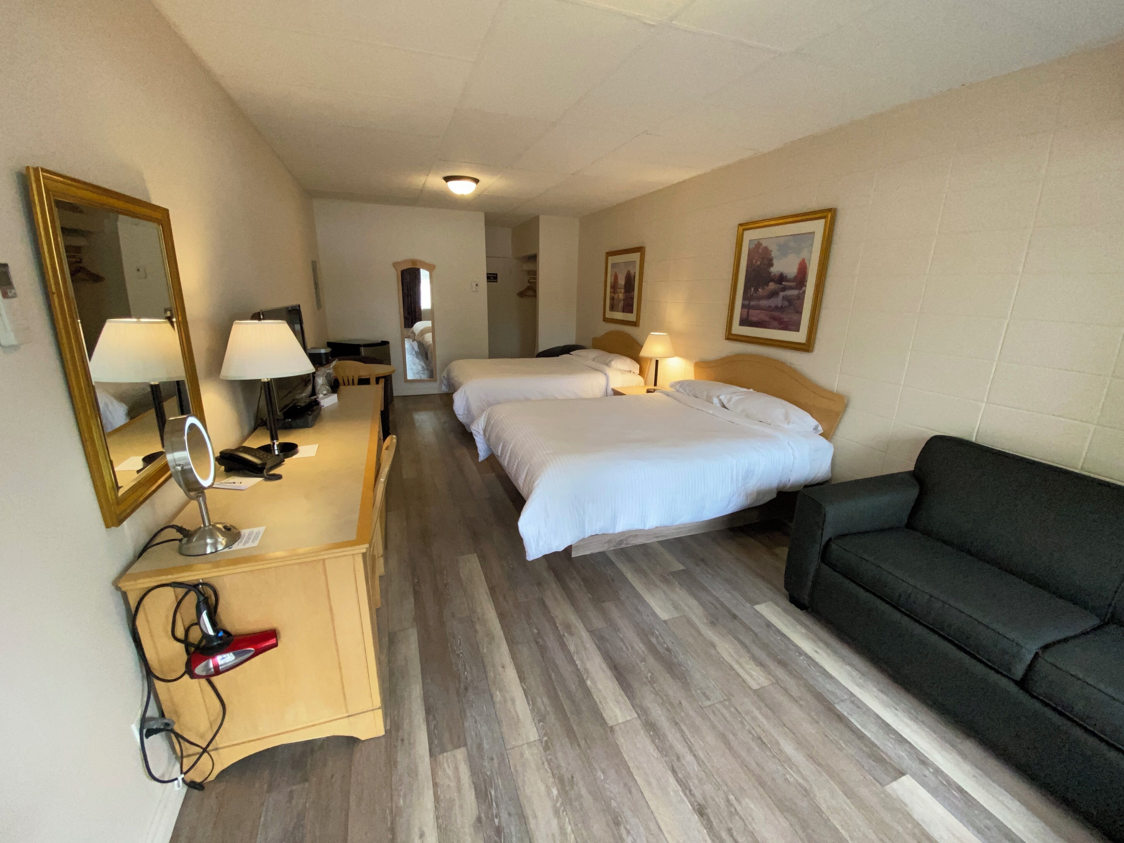 Habitación de hotel con dos camas, un escritorio con espejo, una lámpara y un sofá negro.