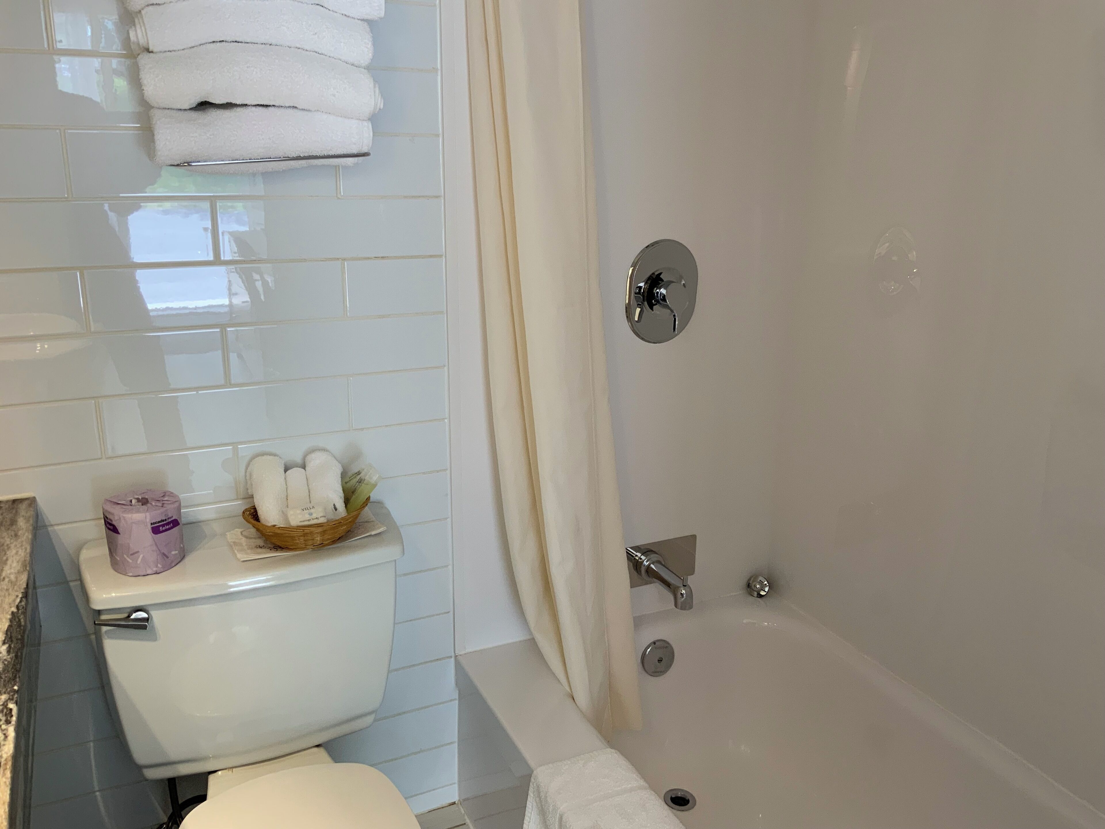 A bathroom with a toilet, a bathtub, and a shelf with towels and toiletries.
