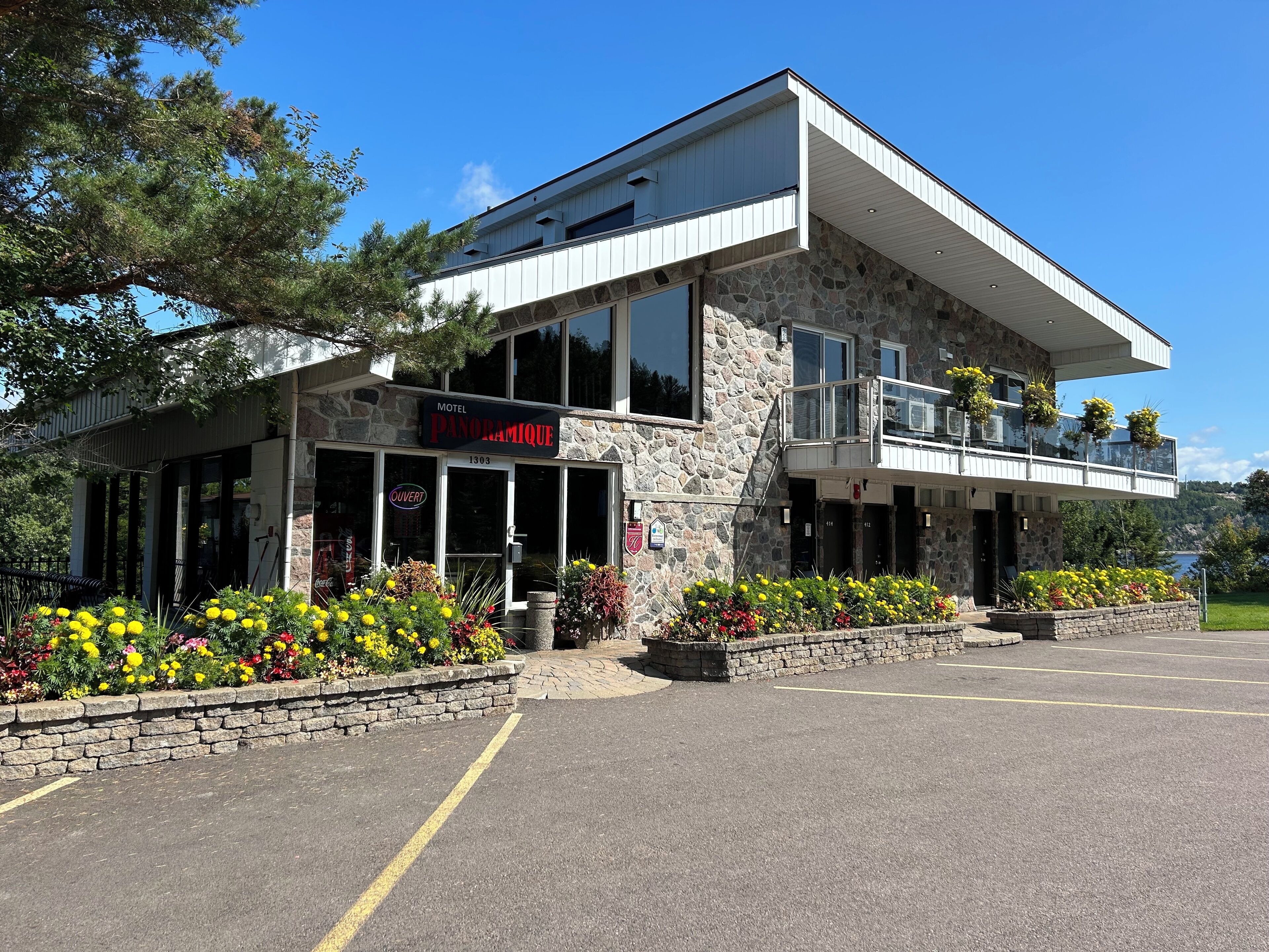 Un motel appelé « Panoramique », doté d’une façade en pierre, de grandes fenêtres et d’un balcon agrémenté de jardinières suspendues.