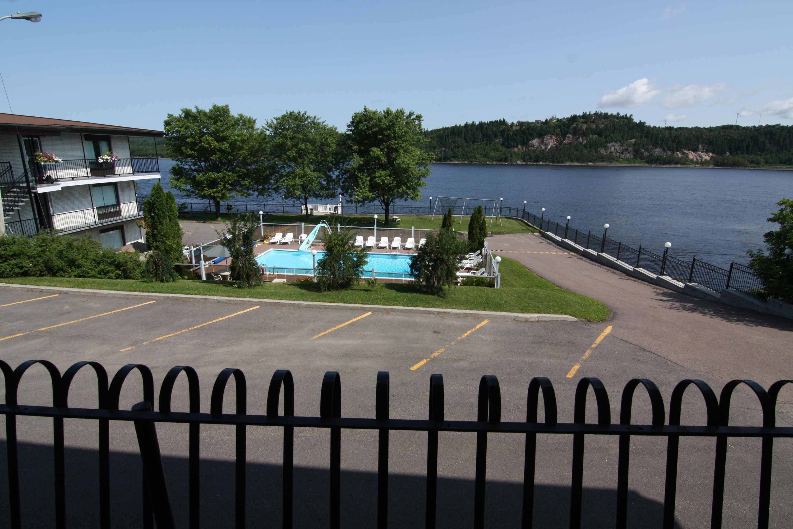 A hotel with a pool, a parking lot, and a view of a lake.