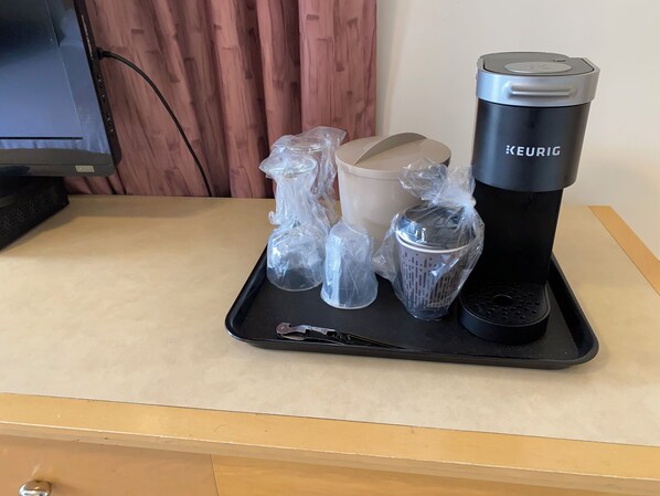 A tray with a Keurig coffee maker, a beige mug, and several plastic containers on a table.
