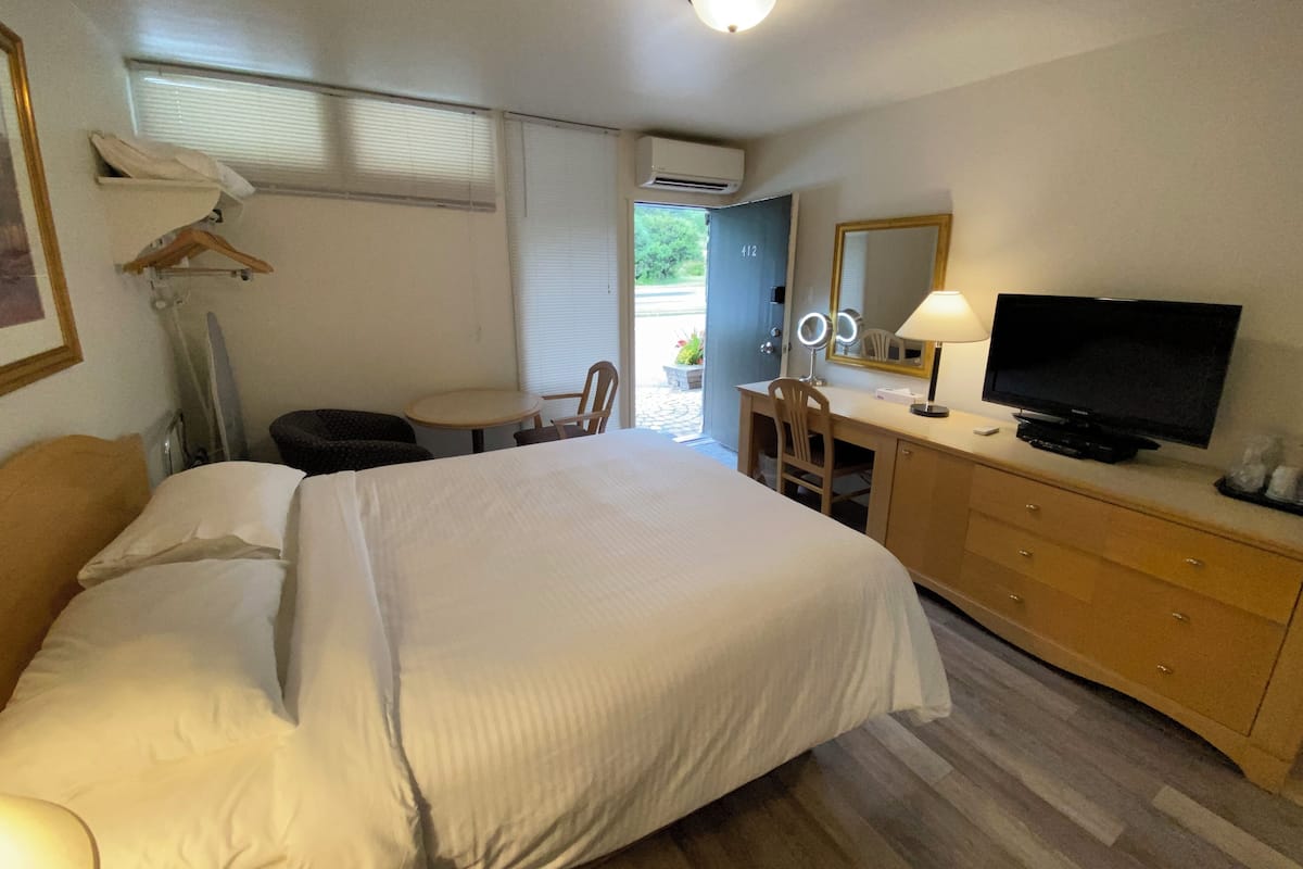 A hotel room with a bed, a desk with a TV, a chair, a dresser, and a window with blinds.