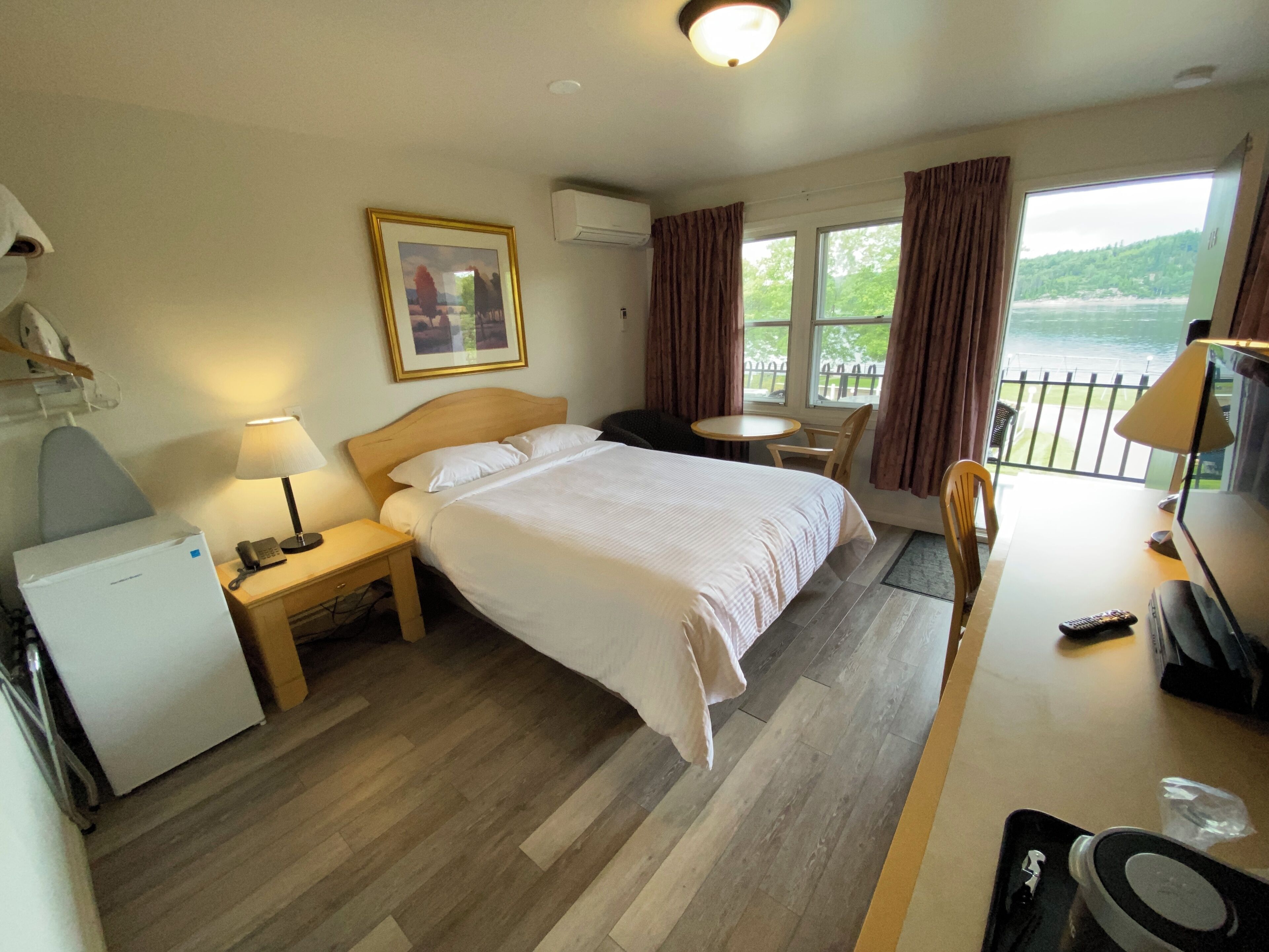 A hotel room with a bed, bedside table, lamp, desk, chair, and a view of the outdoors.