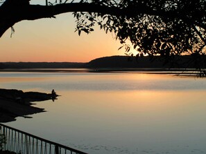 Un lago tranquilo al atardecer con la silueta de una persona en la orilla y una rama de árbol que se extiende sobre el agua.