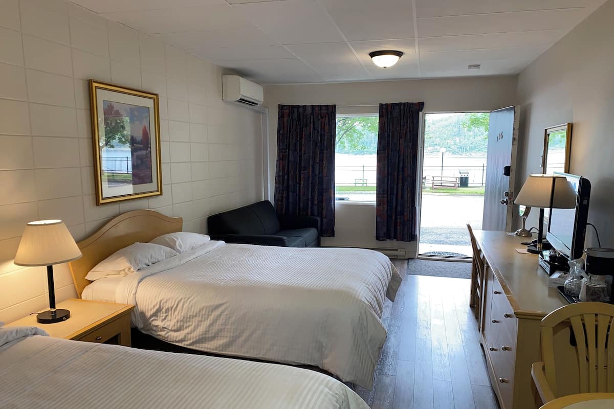 A hotel room with two beds, a desk with a computer, a chair, and a window with curtains.