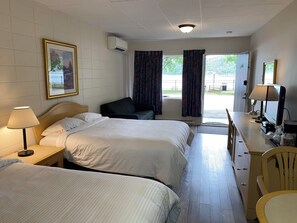 Una habitación de hotel con dos camas, un escritorio con computadora, una silla y un ventanal con cortinas.