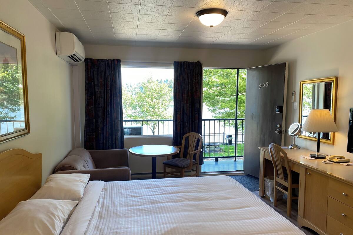 A hotel room with a bed, a desk, a chair, a small round table, and a balcony with curtains.