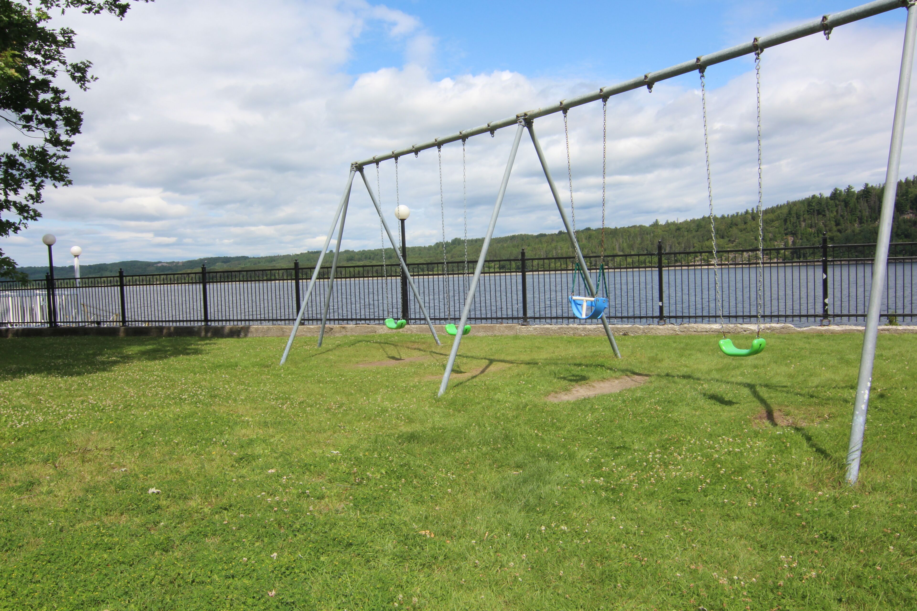 Un parc avec une aire de jeux comprenant des balançoires et une zone délimitée par une clôture.