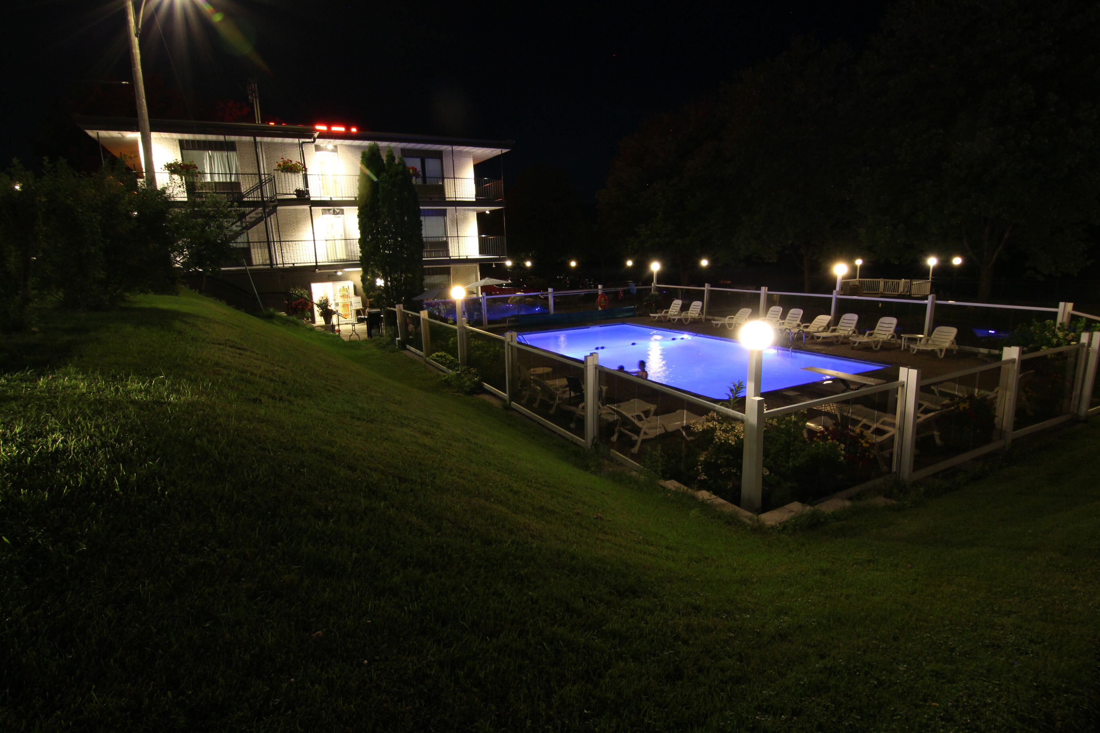 A swimming pool with lounge chairs, surrounded by a fence, and a building with multiple balconies in the background.