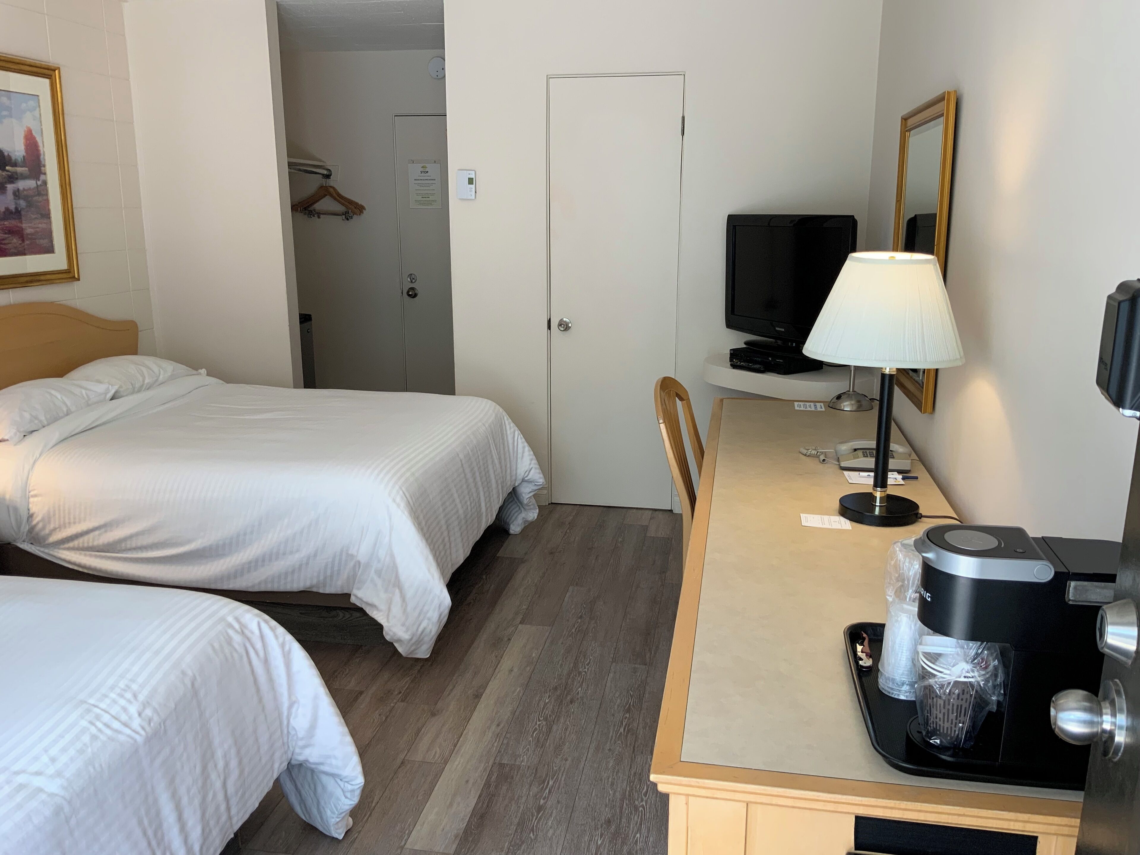 Une chambre d’hôtel avec deux lits, un bureau avec une lampe, une machine à café, une télévision et une porte avec une pancarte.