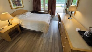 Quarto de hotel com cama, mesas de cabeceira, escrivaninha, cadeira, janela com cortinas e um quadro na parede.