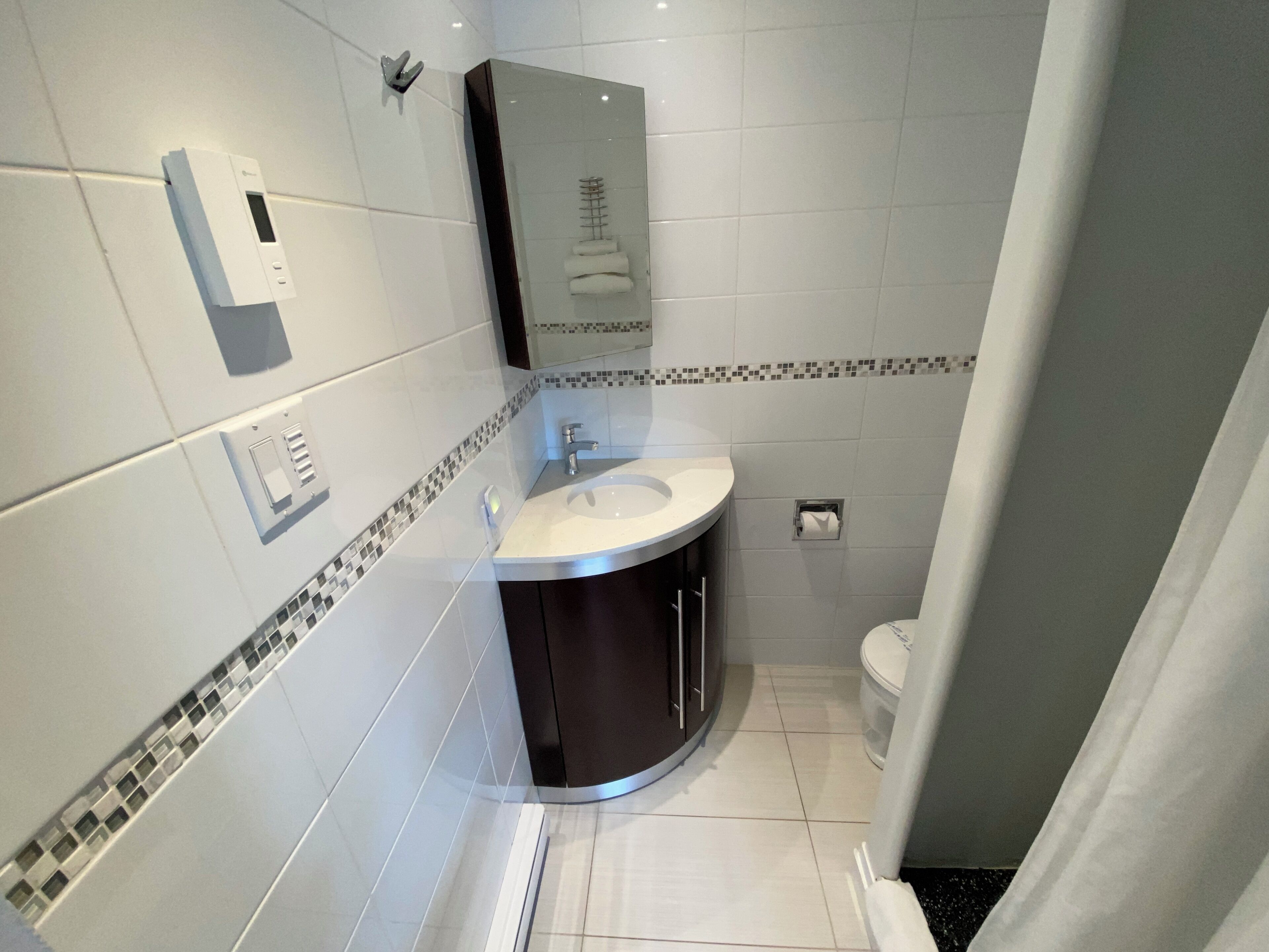 Un baño moderno con un lavabo blanco, muebles oscuros, cabina de ducha de cristal y un inodoro.