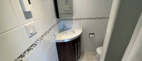 Un baño moderno con un lavabo blanco, muebles oscuros, cabina de ducha de cristal y un inodoro.