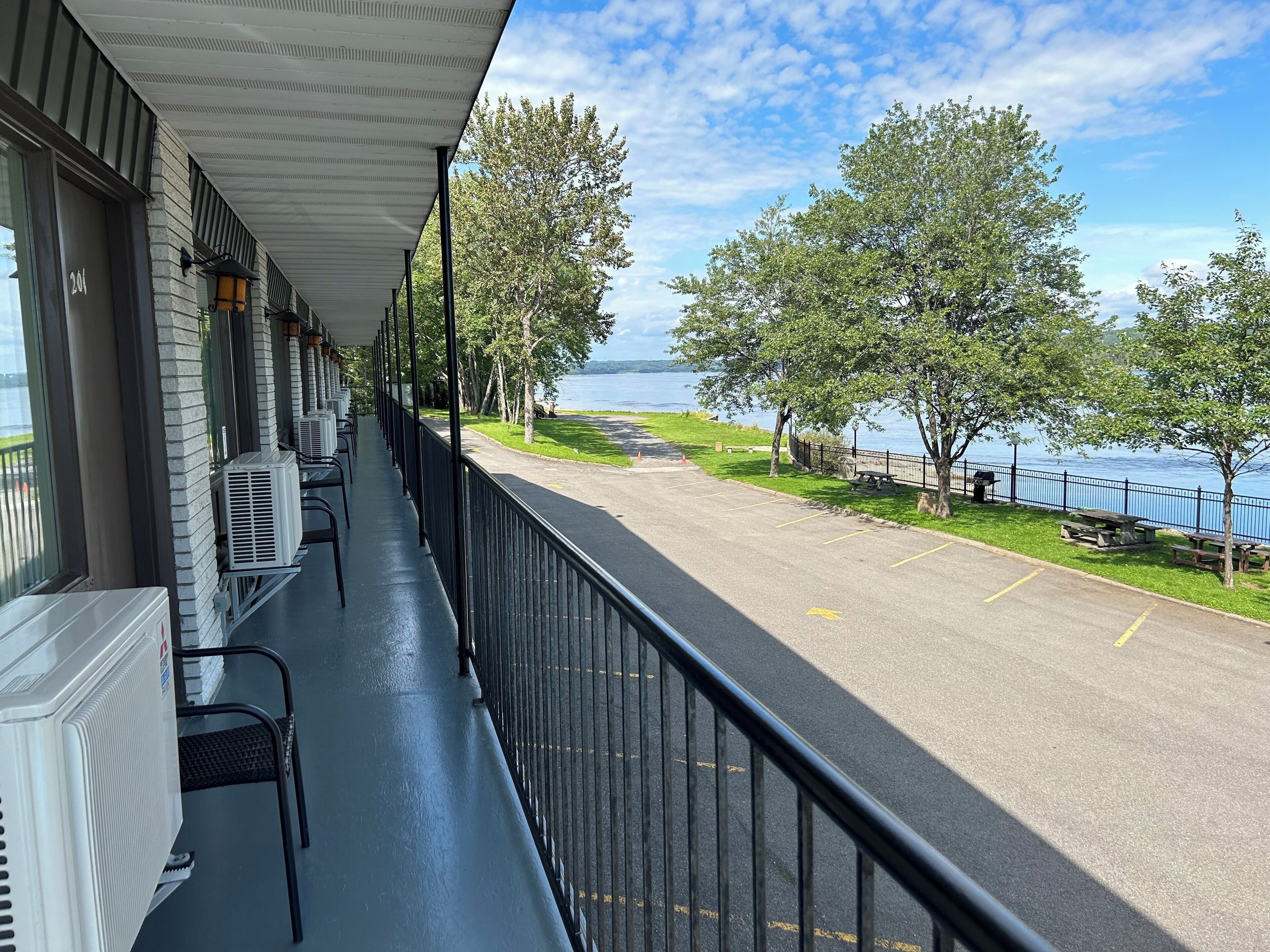 Een balkon met airconditioners, een uitzicht op een parkeerplaats en een meer.