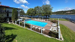 Piscina com espreguiçadeiras, vista para um lago e um edifício com varanda.