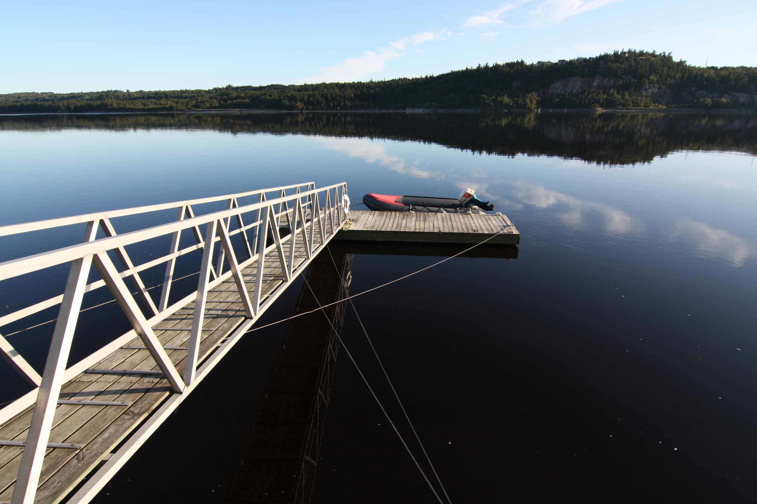 A wooden dock extending into calm water with a clear view of a forested hill in the background.