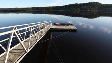 A wooden dock extending into calm water with a clear view of a forested hill in the background.