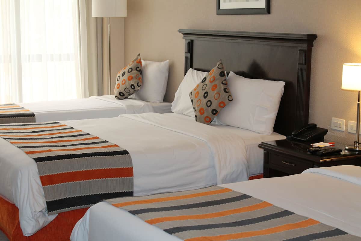 A hotel room with two beds, each with a striped blanket, a nightstand with a phone, and a lamp.