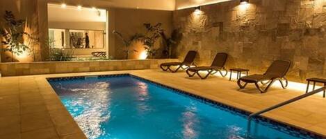 Une piscine avec des chaises longues et un mur en pierre.