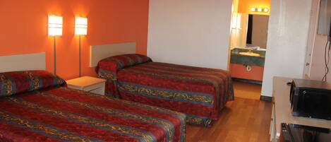 A hotel room with two beds, a nightstand, a dresser, a microwave, and a bathroom visible through an open door.
