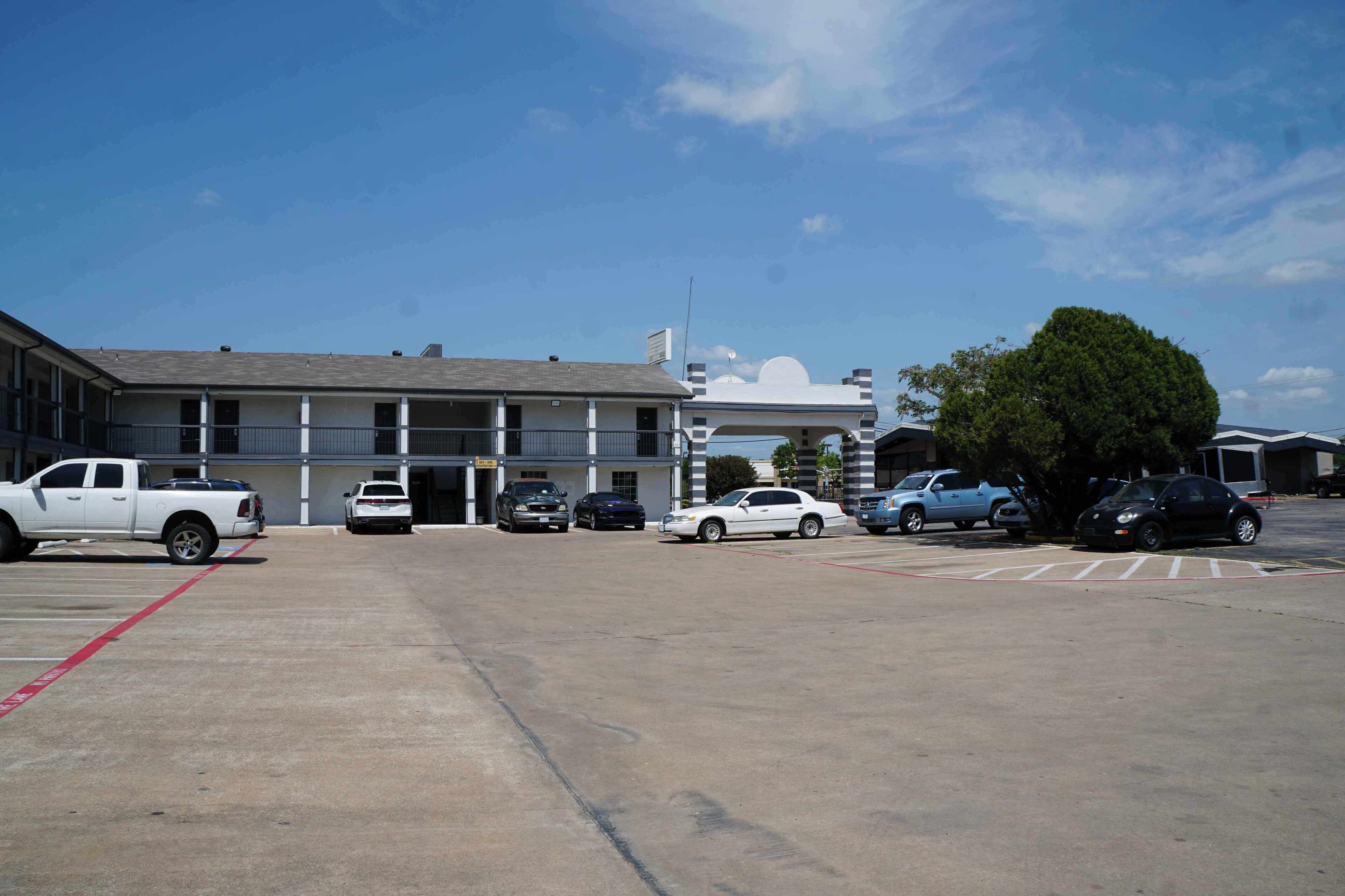 A parking lot with several cars and a building with a flat roof and a sign.