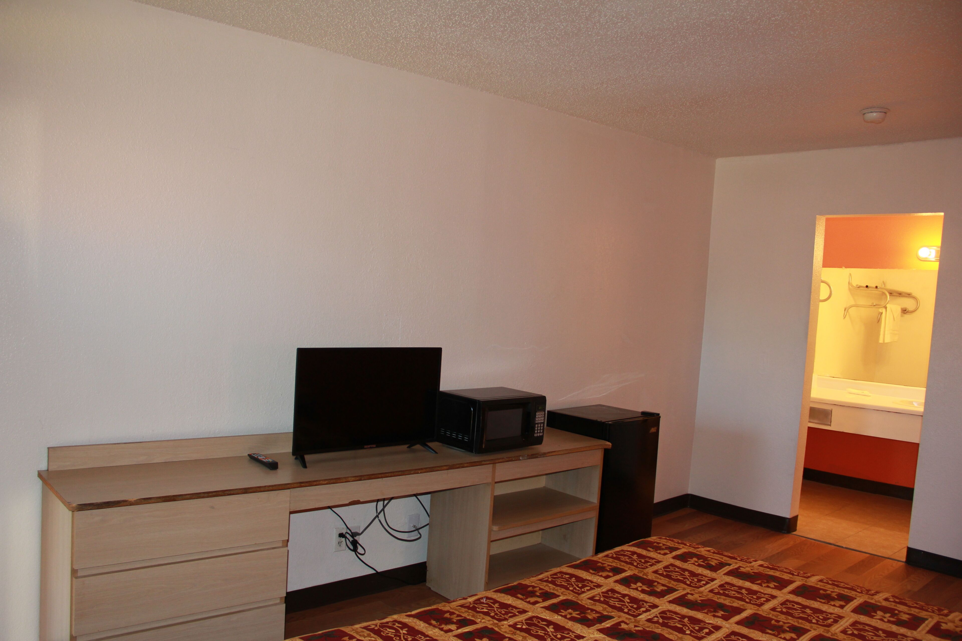 A small room with a wooden desk, a black monitor, a microwave, and a red patterned rug.