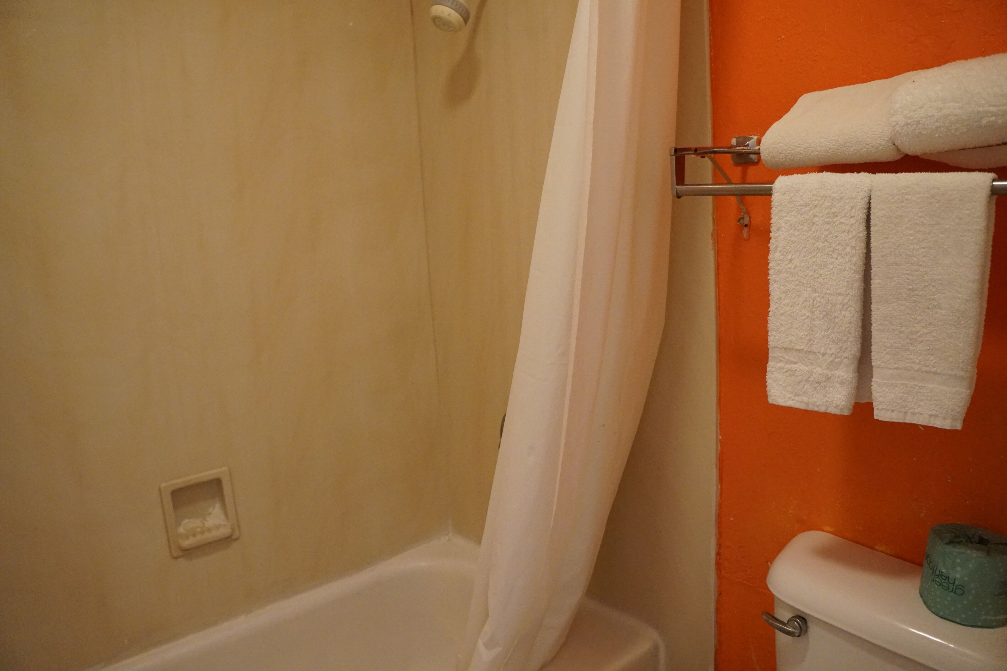 A bathroom with a bathtub, a toilet, and a towel rack with two towels.