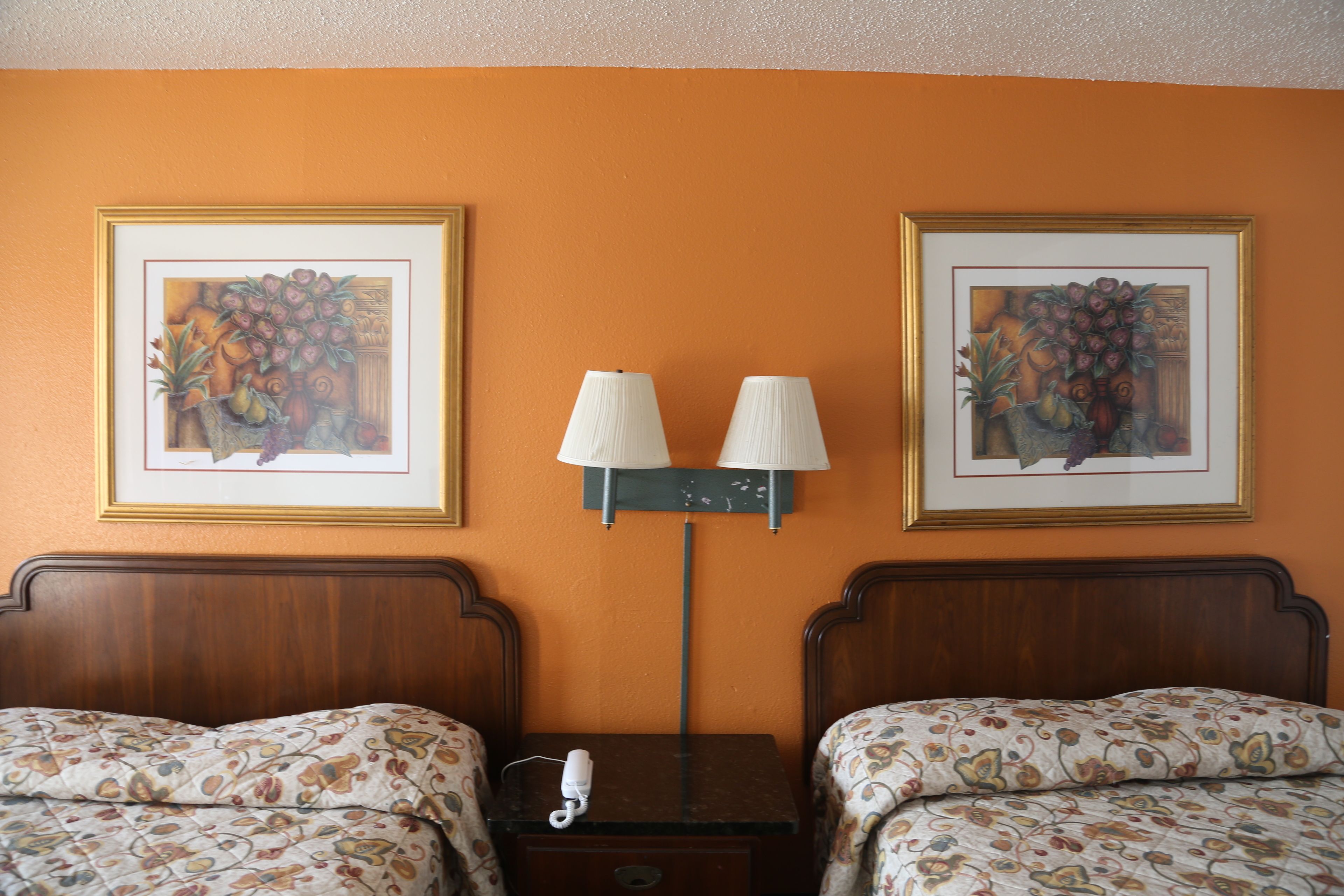 Habitación de hotel con dos camas, una mesita de noche, una lámpara y dos cuadros enmarcados con motivos florales en la pared.