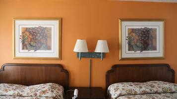 Habitación de hotel con dos camas, una mesita de noche, una lámpara y dos cuadros enmarcados con motivos florales en la pared.