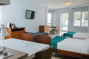 A modern hotel room with a wooden desk, a comfortable sofa, a bed with a teal blanket, and a TV mounted on the wall.