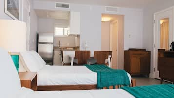 Habitación de hotel con dos camas, kitchenette, escritorio y una silla.