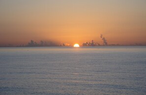 A sunset over a calm body of water with a distant shoreline. - Tides Inn Hotel (Lauderdale-by-the-Sea)