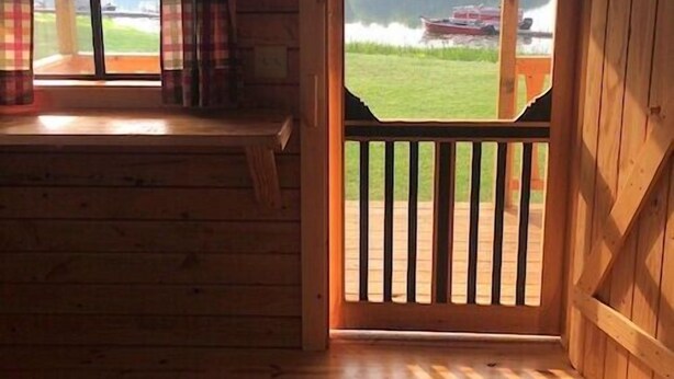 A cabin with a wooden interior, a sliding glass door leading to a deck, and a view of a lake with a boat. - Duck Lake Campground (Red Creek)