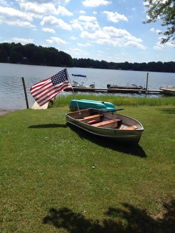 A small boat with a registration number on a grassy area near a body of water, an American flag, and a rowboat with a blue cover. - Duck Lake Campground (Red Creek)