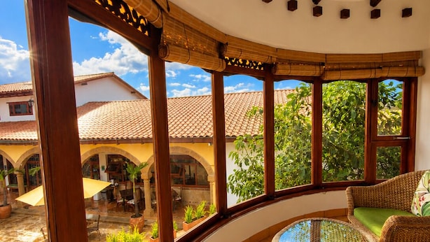 A curved balcony with wicker furniture, a glass table, and a view of a courtyard with plants and a building.