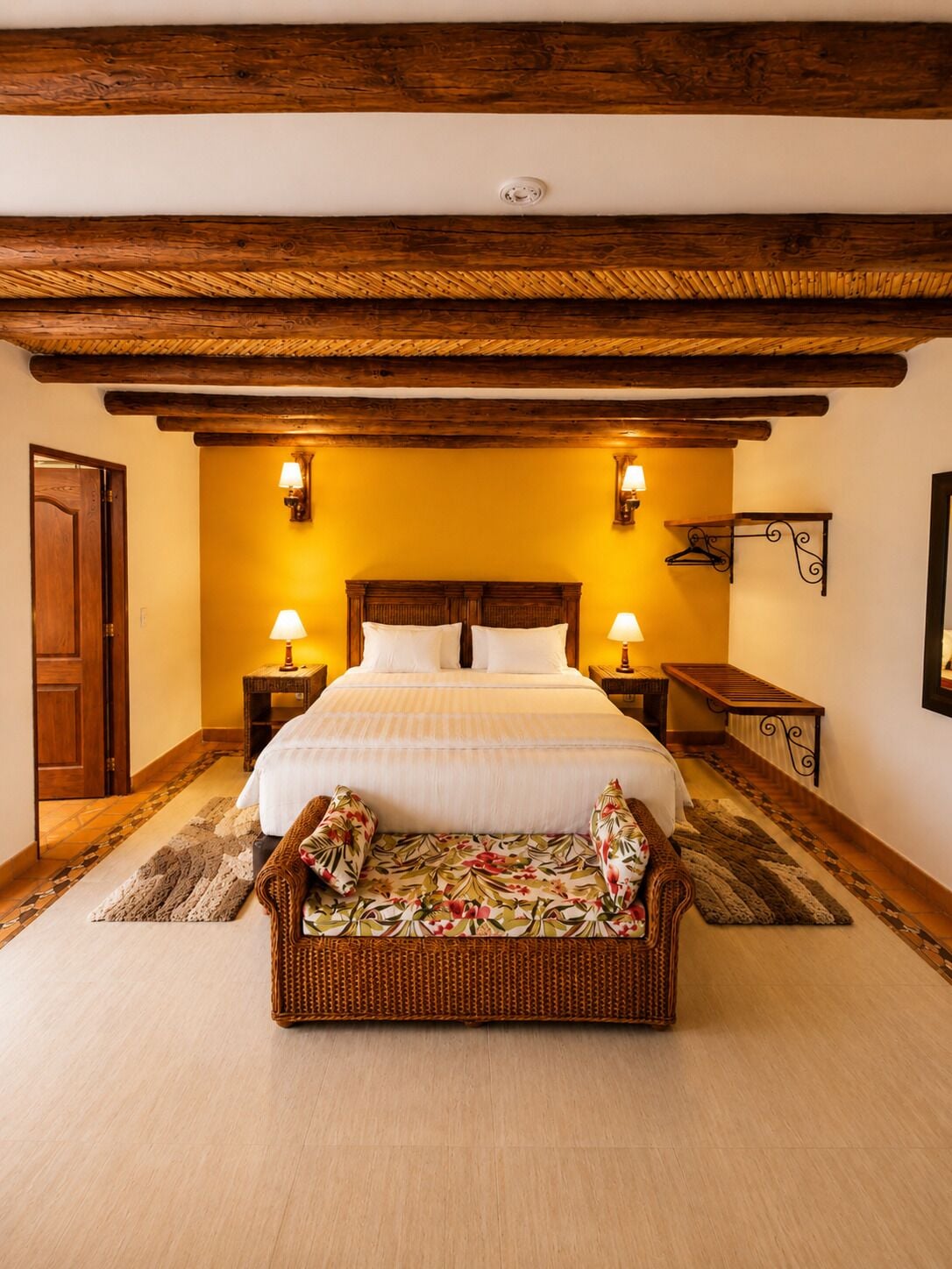 A room with a wooden ceiling, a bed with white linens, two bedside lamps, a wicker sofa, and a wooden bench.