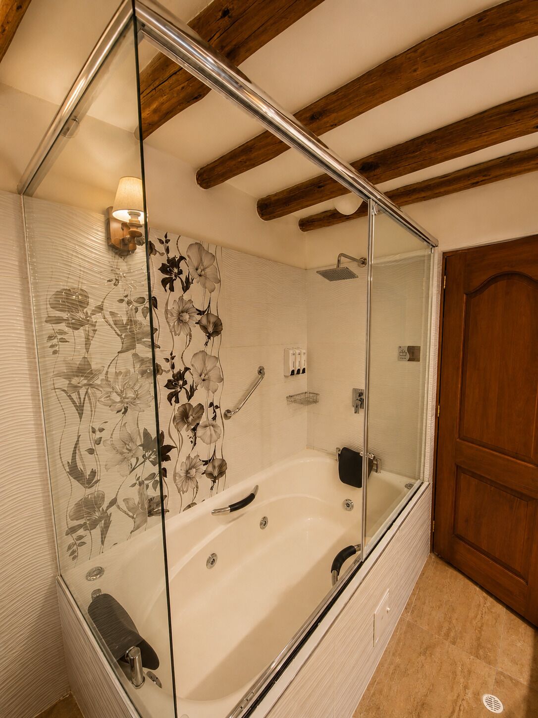 A bathroom with a glass-enclosed bathtub, wooden ceiling beams, and a floral wall design.