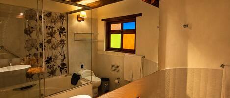 A bathroom with a large mirror, wooden vanity, and a window with colored panes.