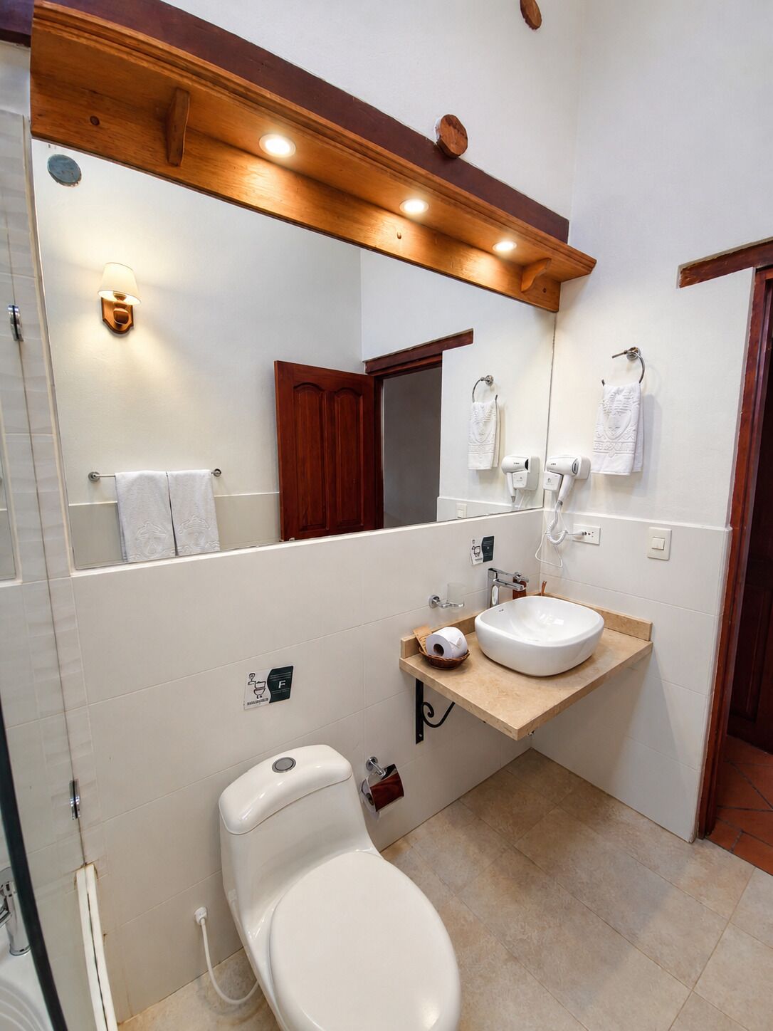 A bathroom with a wooden vanity, a large mirror, a toilet, and a shower area.