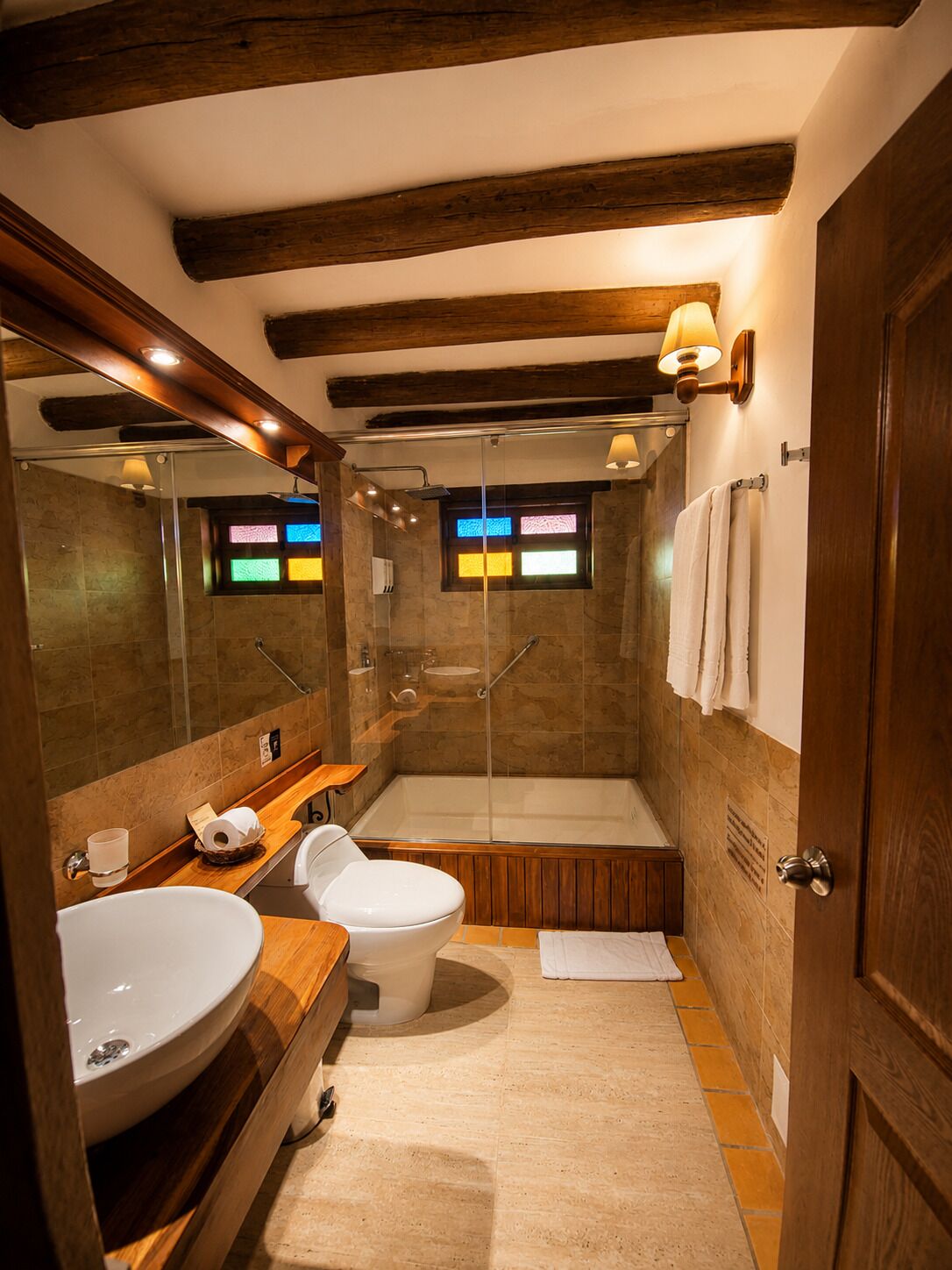 A modern bathroom with a wooden vanity, a toilet, a glass-enclosed shower, and a large mirror.
