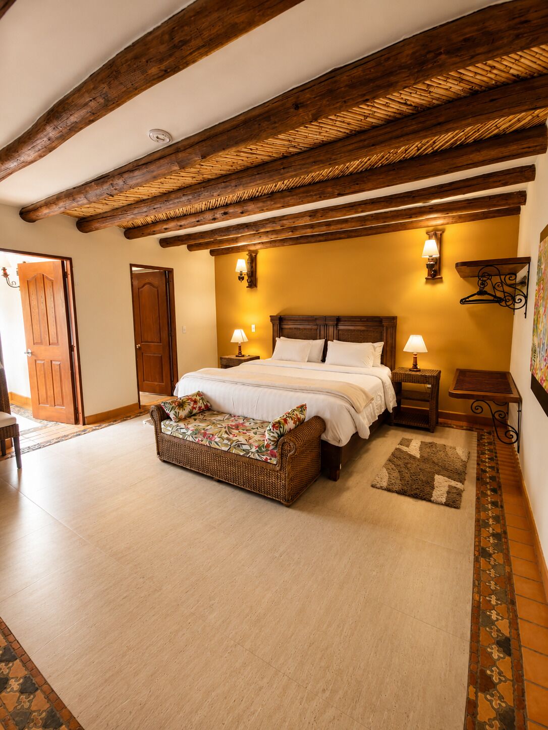 A bedroom with a bed, bedside tables, a wicker bench, and a patterned rug.