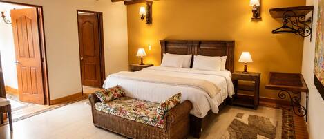 A bedroom with a bed, bedside tables, a wicker bench, and a patterned rug.