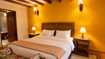 A room with a large bed, two bedside tables with lamps, a wicker bench, and a wooden ceiling.