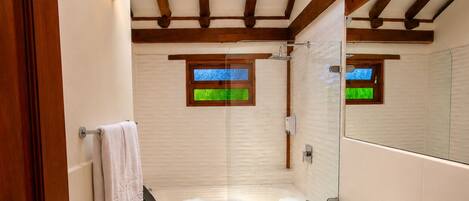 A bathroom with a bathtub, toilet, and sink, wooden beams on the ceiling, and a window with a view.