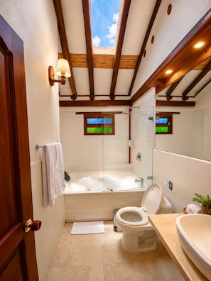Un baño con bañera, inodoro y lavabo, vigas de madera en el techo y una ventana con vistas.