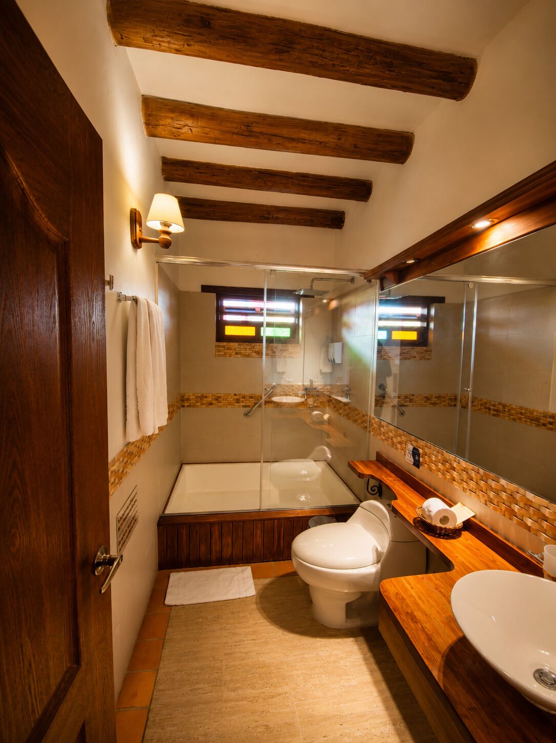 A bathroom with a bathtub, toilet, and sink, wooden beams on the ceiling, and a mirror above the sink.