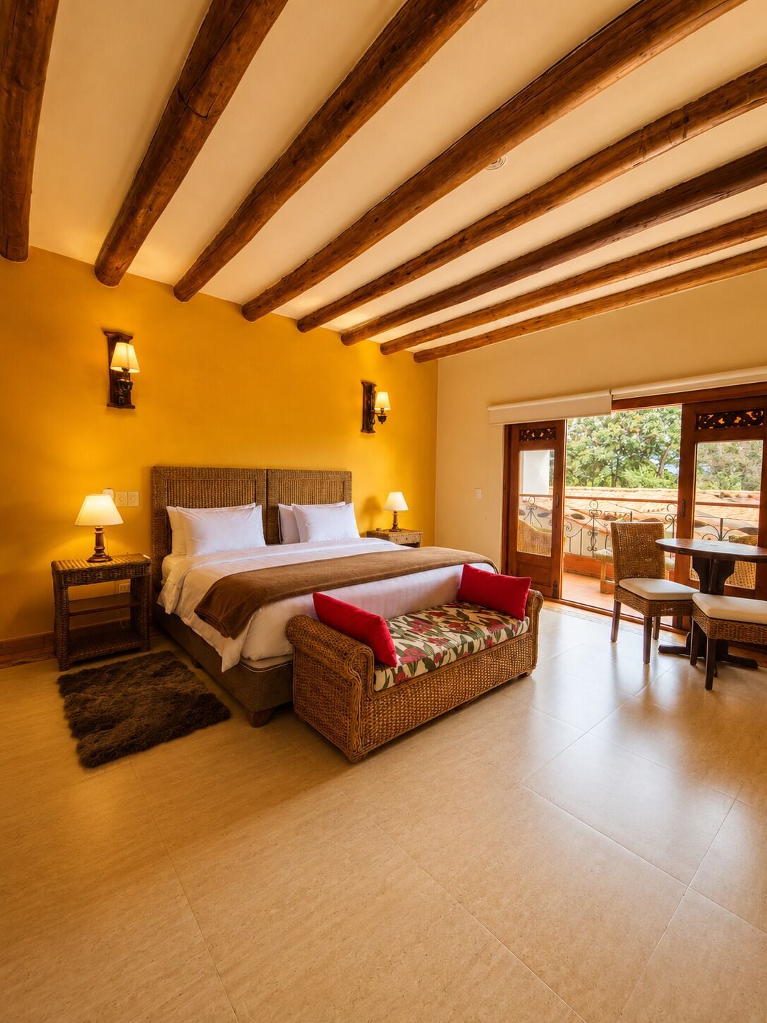 Un dormitorio con cama, lámparas de noche, un sofá de mimbre, una mesa de comedor y vistas al exterior.