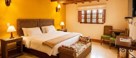 A bedroom with a bed, bedside lamps, a window, a chair, a table, and a television.