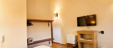 A bedroom with a bed, a television, a small heater, and a wooden shelf.