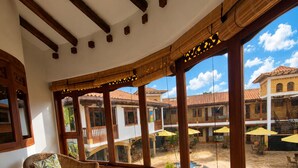 A room with wicker furniture, large windows, and a view of a courtyard with buildings.